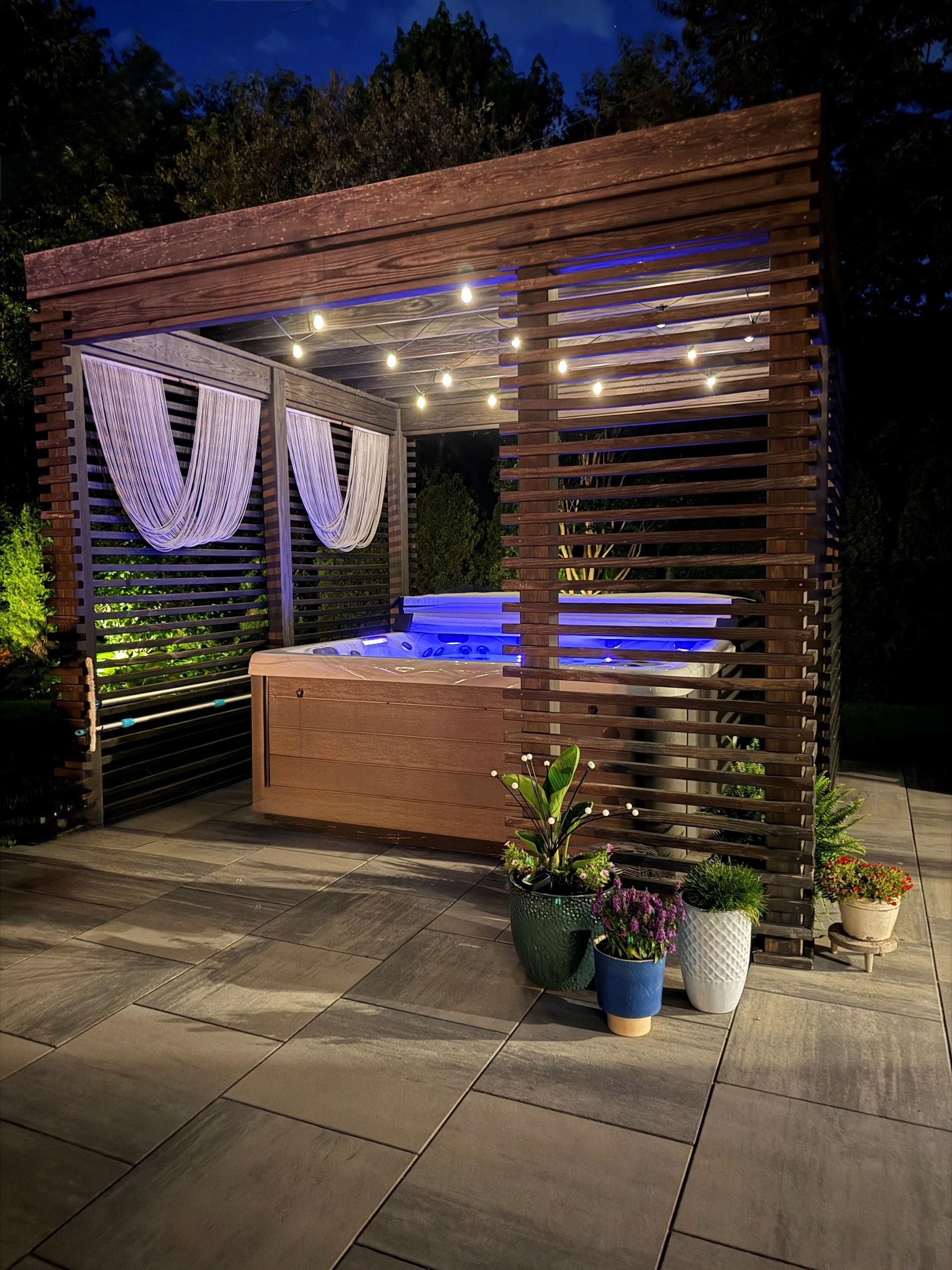 Gorgeous, luxury modern boho backyard design showcasing an outdoor pergola made from pine at sunset with a hot tub.